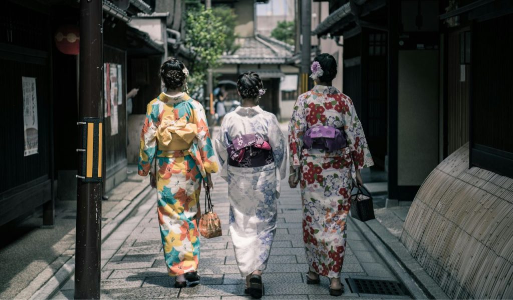 Three Geisha Walking Between Buildings
