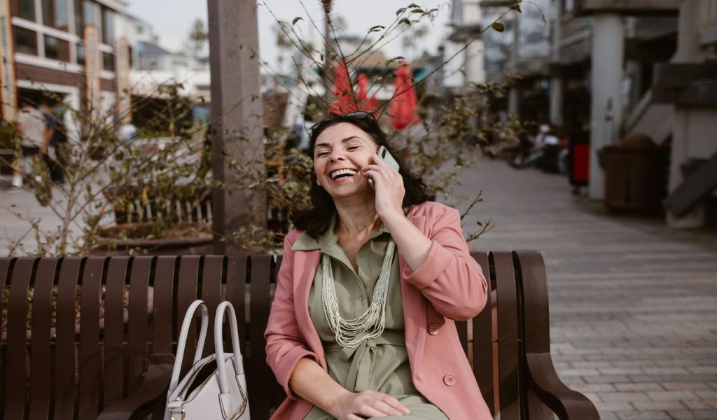 Femme portant des manches longues roses assise sur un banc en bois tout en passant un appel téléphonique