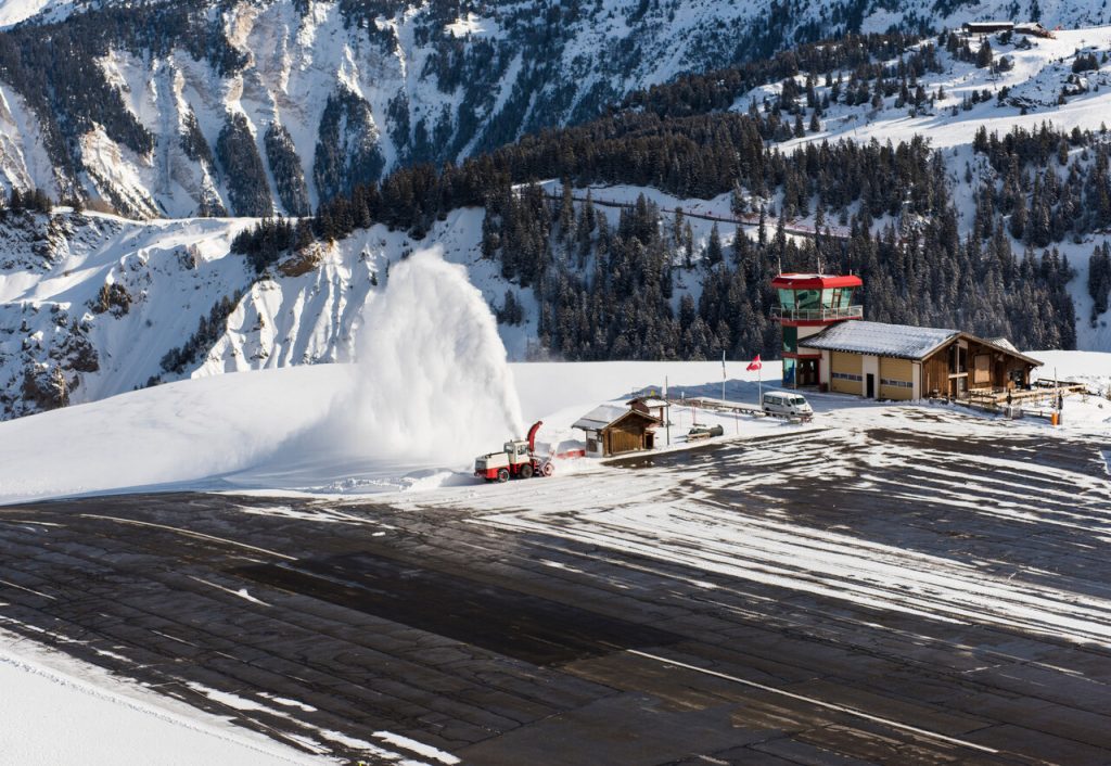 Small airport altiport runway being cleared of snow by blower on the side of an alpine mountain in winter