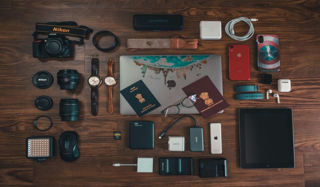 Passports, Camera, Battery Charger, Watches, and Cables on Brown Wooden Surface
