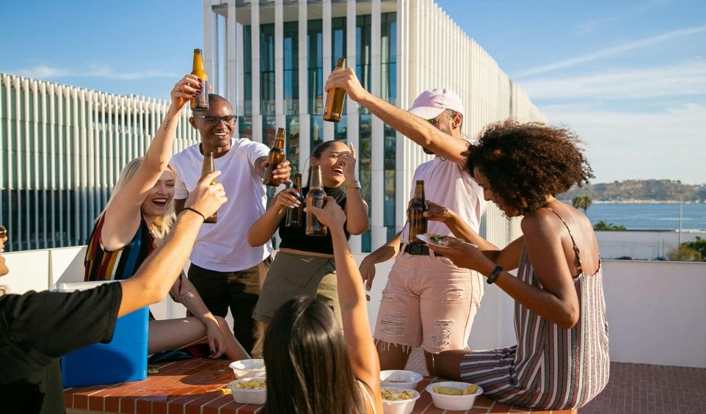 11 U.S. Cities Beer Lovers Should Put on the Map – Her Life Adventures Joyful diverse friends toasting with beer bottles on rooftop