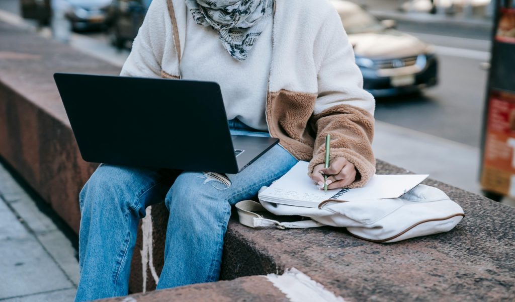 Anonymous female using laptop and taking notes on street
