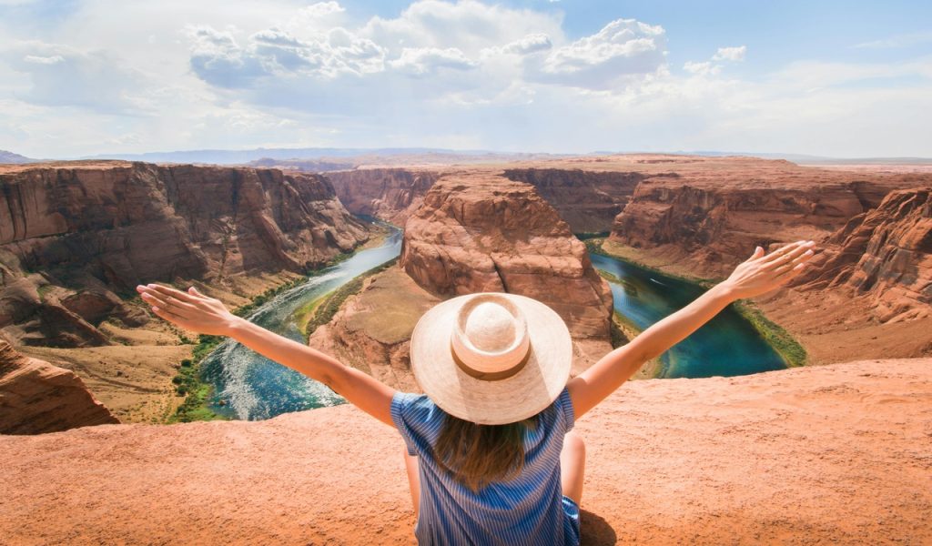 15 Bucket-List Destinations Frequent Travelers Love – Her Life Adventures Woman Sitting on Cliff Overlooking Mountain