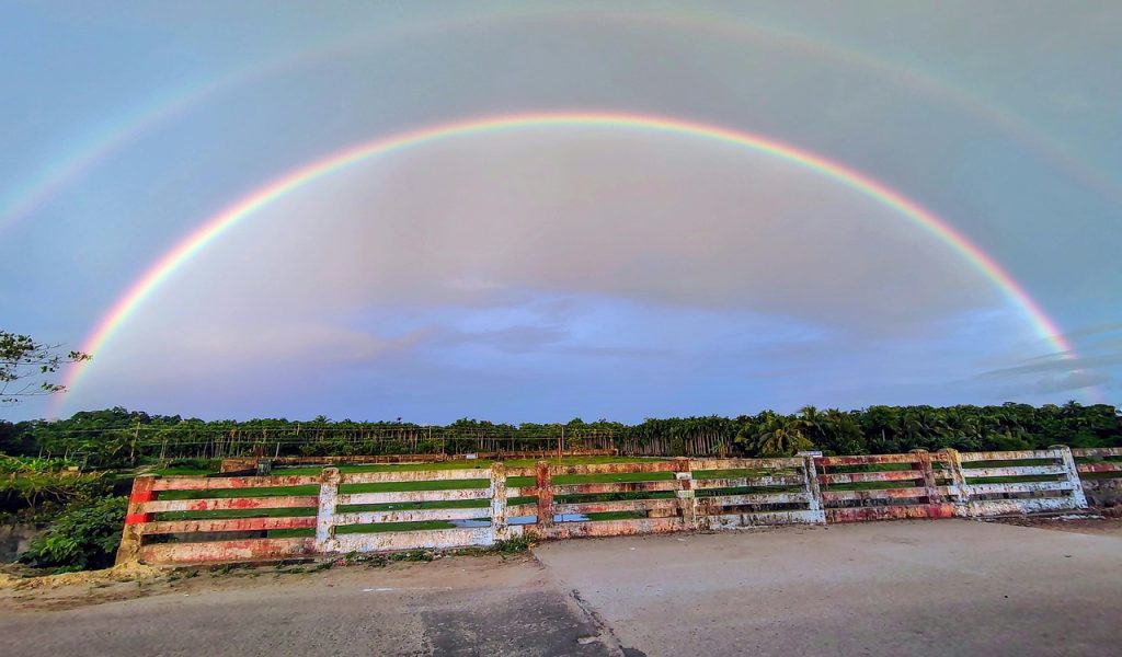 Vibrant Double Rainbow Over Rustic Countryside Bridge
