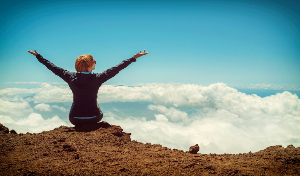 Person Sitting on Cliff Raising Up Both Hands 