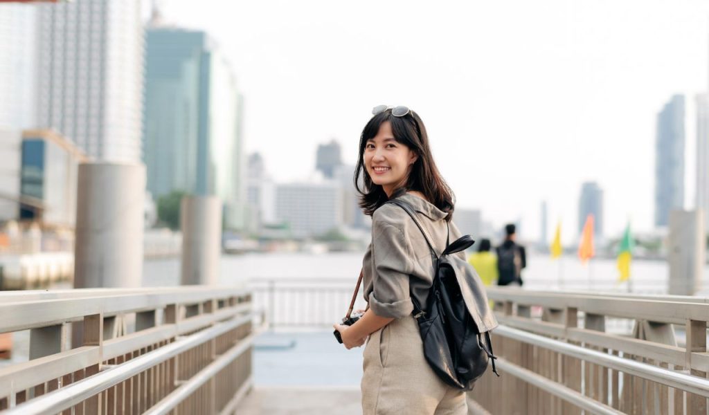 Young Asian woman backpack traveler waiting an express boat at pier on Chao Phraya River in Bangkok. Journey trip lifestyle, world travel explorer