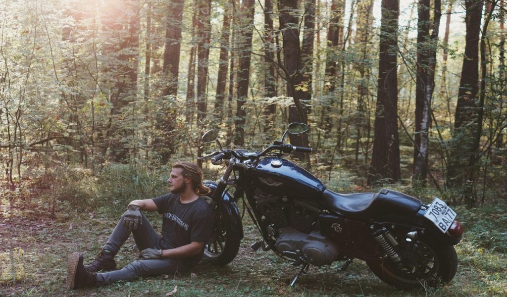 Man Sitting on the Ground Leaning Back on Parked Motorcycle
