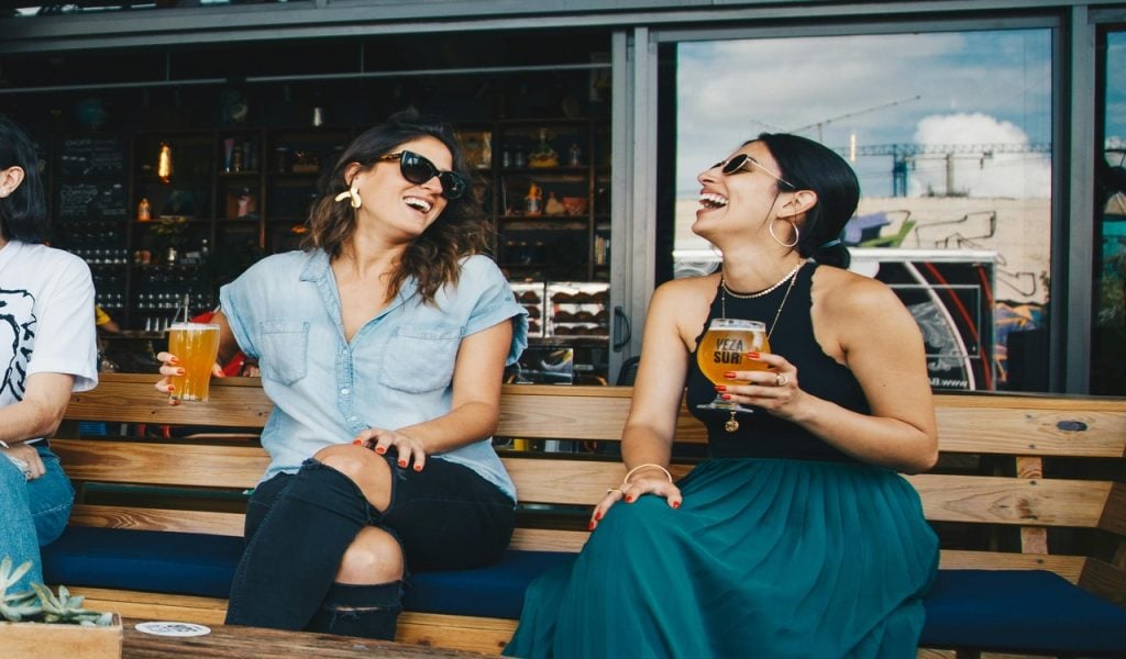 11 U.S. Cities Beer Lovers Should Put on the Map – Her Life Adventures Two Smiling Women Sitting on Wooden Bench