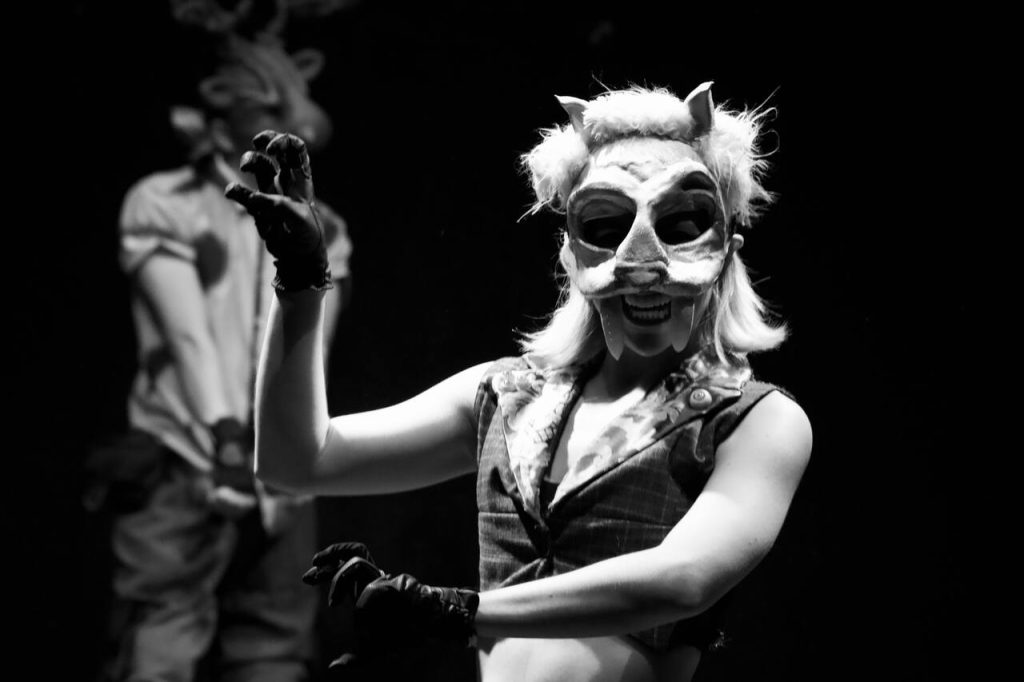 Masked audience members walking through dim, theatrical rooms.