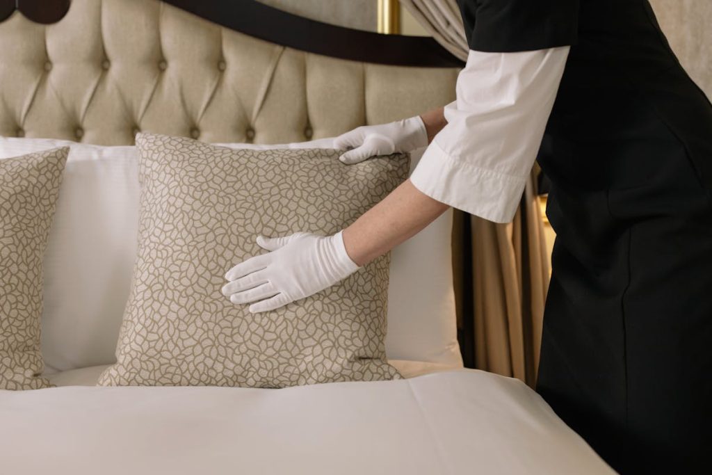 Woman with White Gloves Arranging a Pillow on Bed
