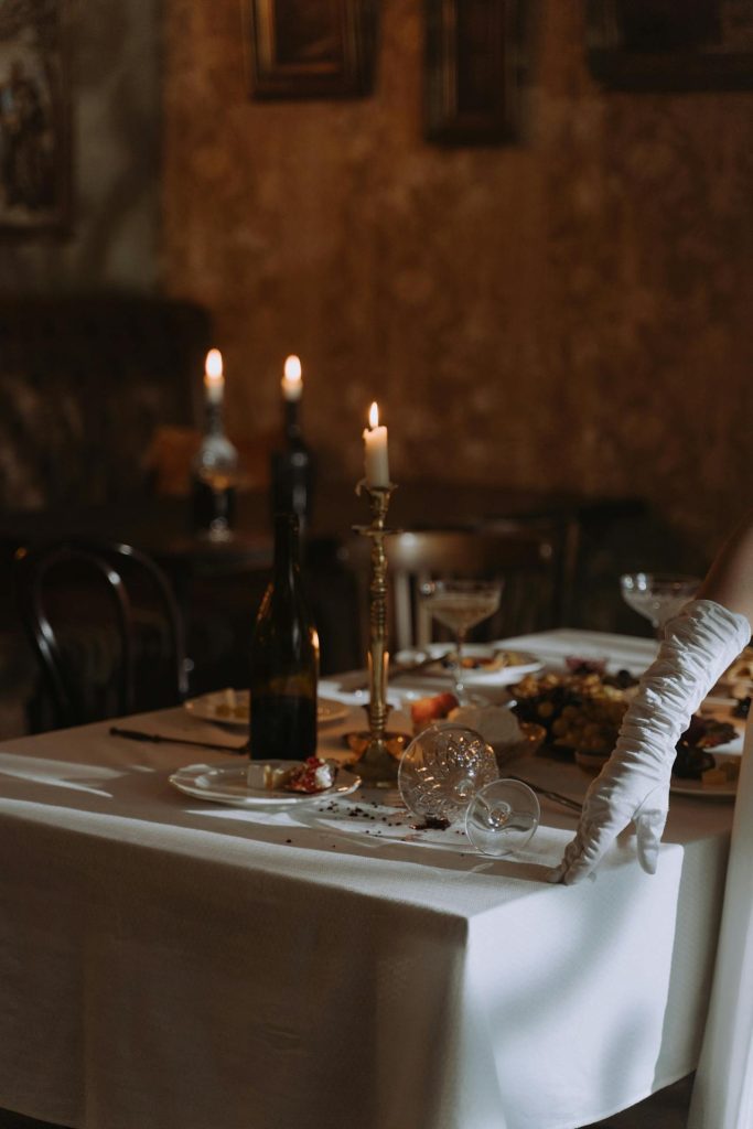 A candlelit dining table inside a vintage mansion, with antique furniture, silverware, and ghostly lighting