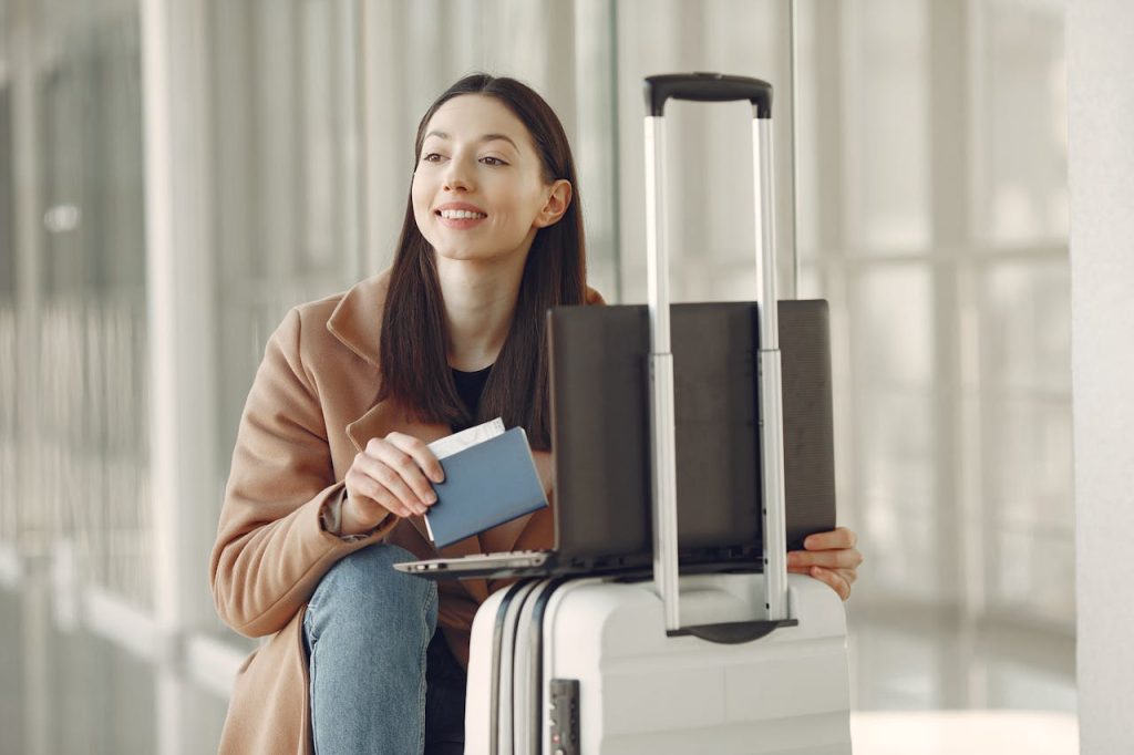 A traveler holding a smartphone and passport at an airport terminal, with digital boarding gates in the background.