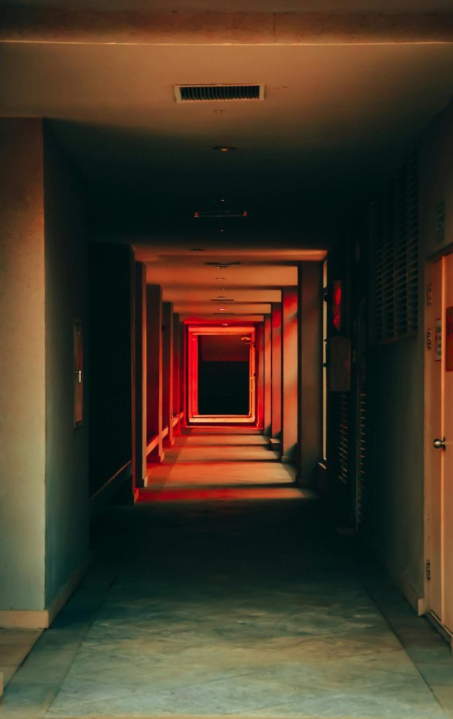 A dark, industrial-looking hallway with red lighting.