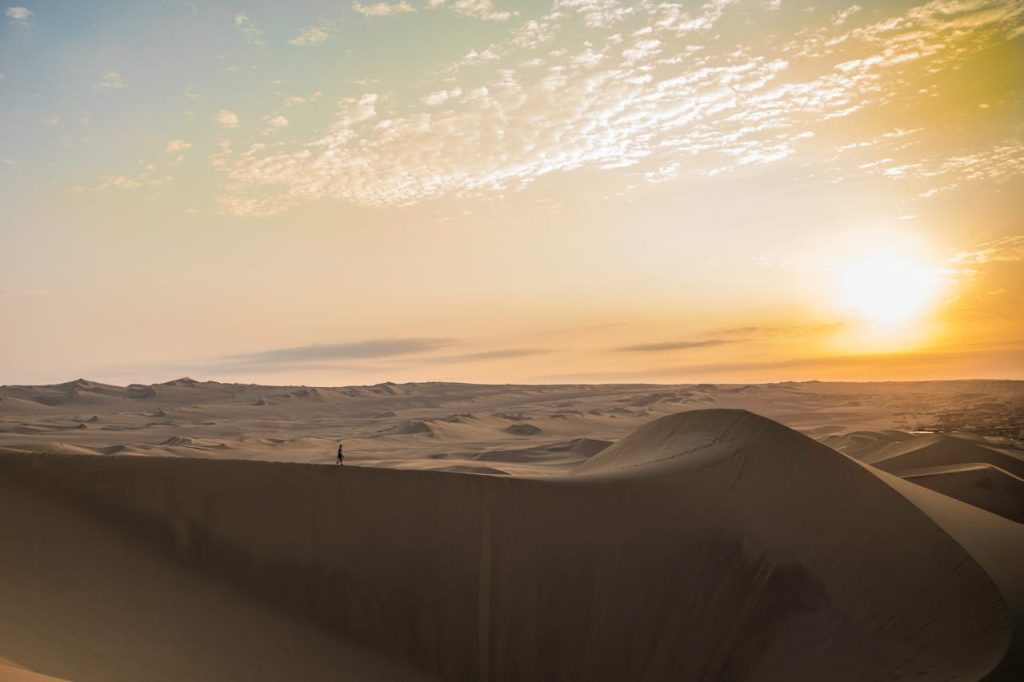 A Person Walking on a Desert During Sunset
