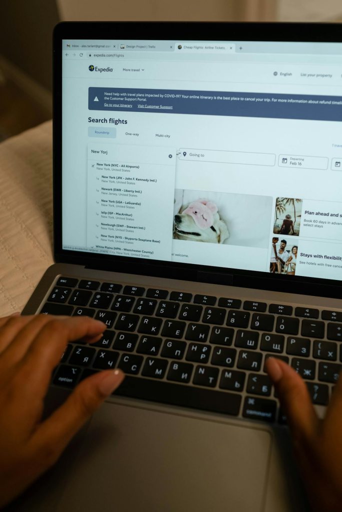 A traveler booking flights on a laptop in the morning light.