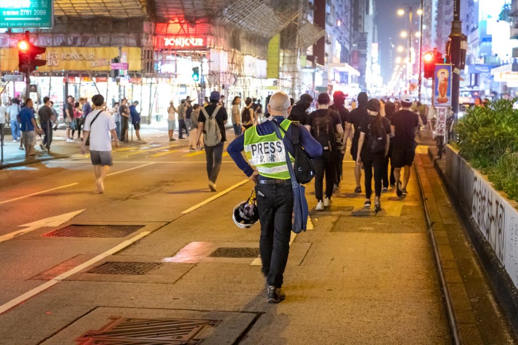 Nighttime street lined with neon signs and crowds gathering outside loud bars and clubs.