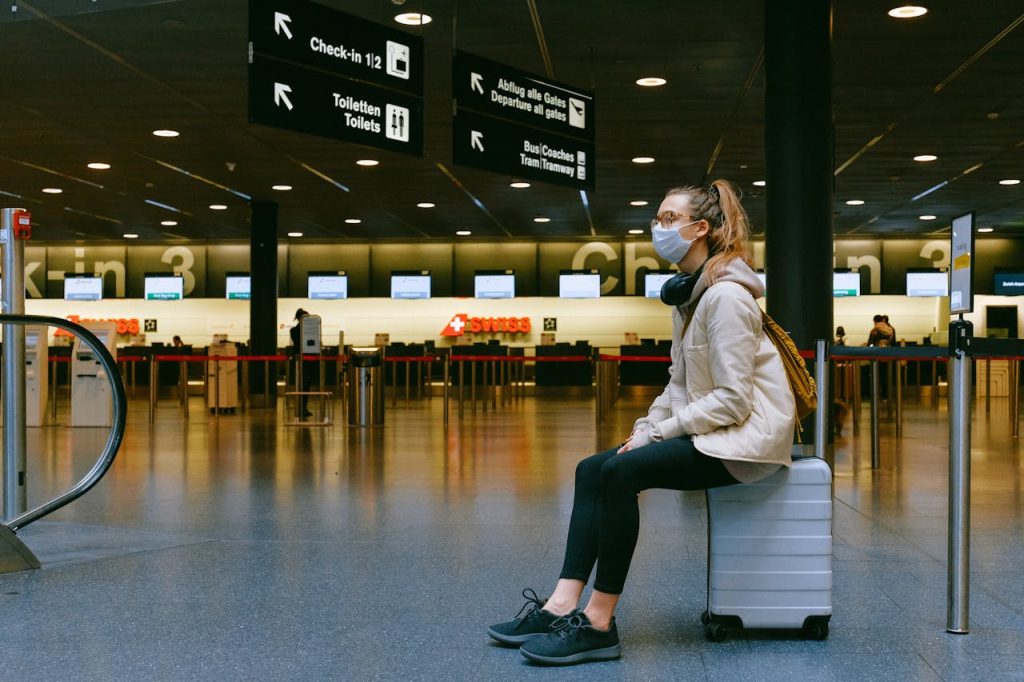 A traveler at the airport wearing a jacket and sturdy shoes while holding a lighter carry on.