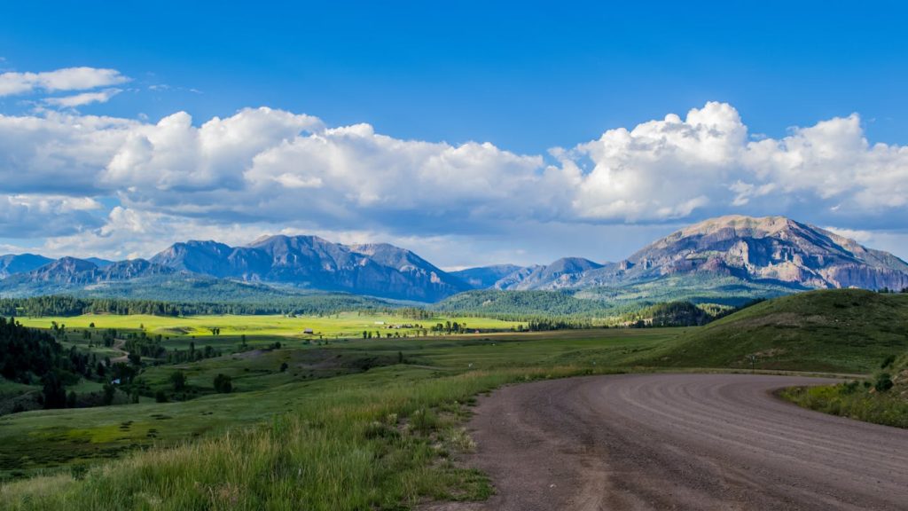 Green Grass Field near Mountains under the Cloudy Blue Sky

