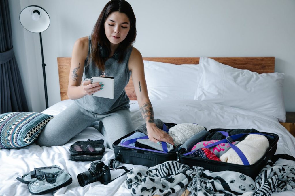 A traveler checking items off a packing list on a phone or notebook beside an open suitcase.