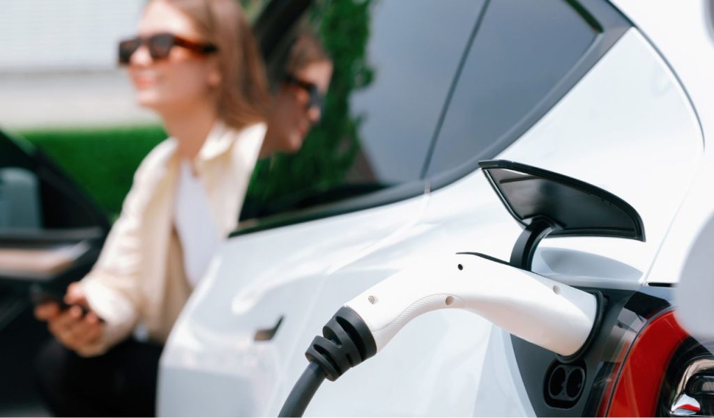 Young woman use smartphone to pay for electricity at public EV car charging station green city park. Modern environmental and sustainable urban lifestyle with EV vehicle. Expedient