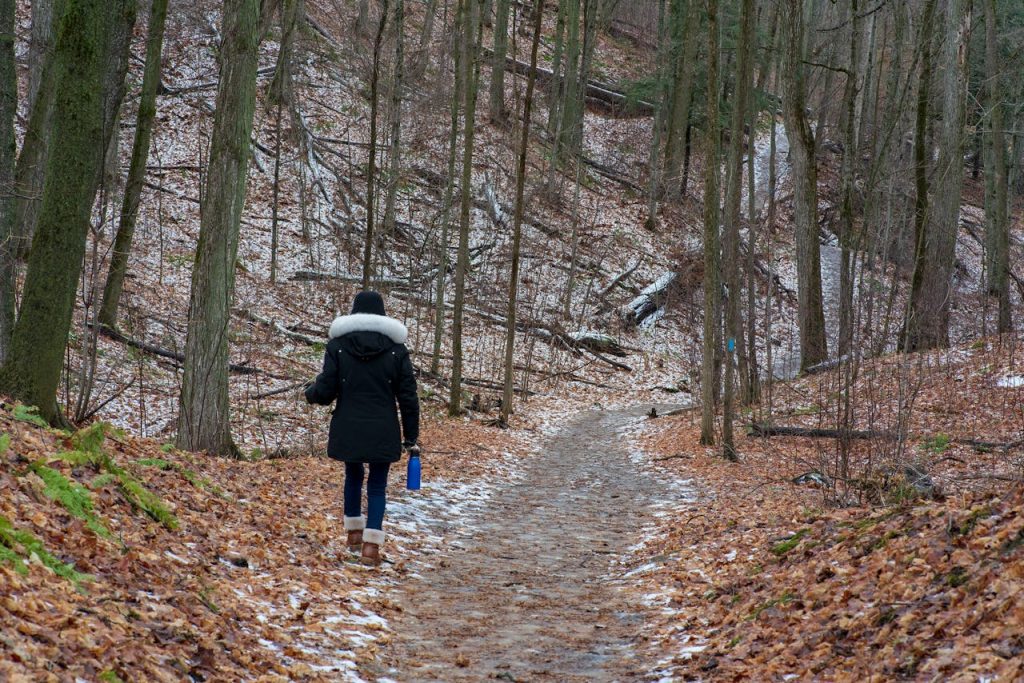 A traveler walking along a forested trail with a reusable bottle clipped to their pack