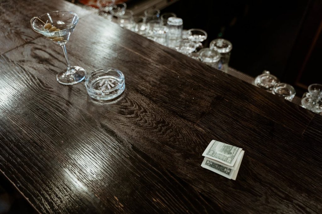 Dollar Bills on a Wooden Table Beside an Ashtray and a Wine Glass 