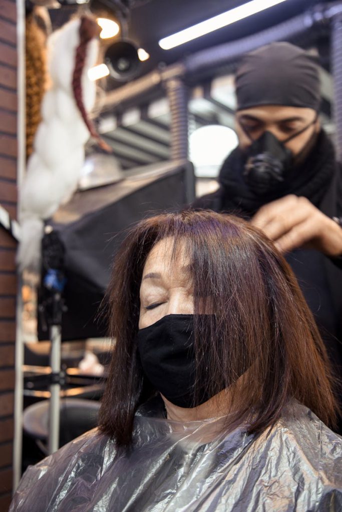 Man in black respirator dying hair of aged woman