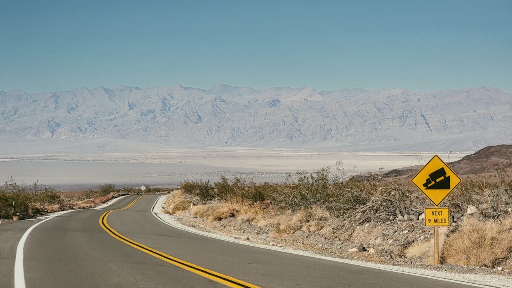 A road with a yellow sign on it and mountains in the background