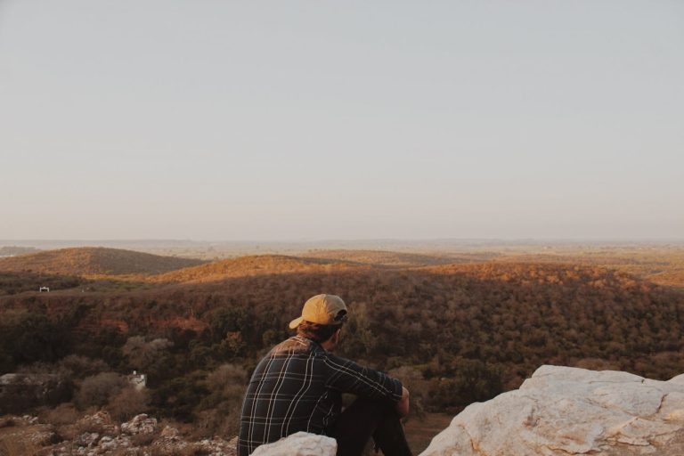 Man in Black and White Plaid Dress Shirt Sitting on Rock