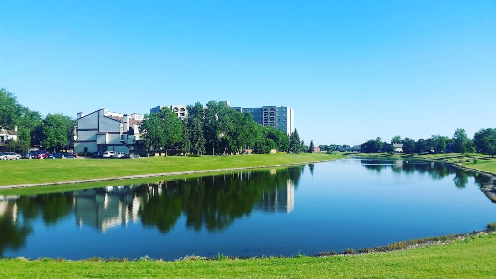 Body of Water Surrounded by Grass Near Buildings in Winnipeg, MB, Canada