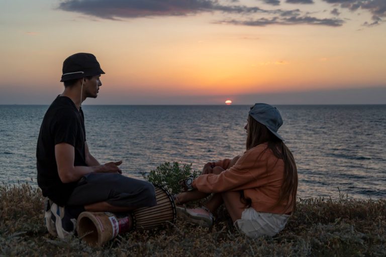 Man with a Drum Sitting Near the Sea During Sunset
