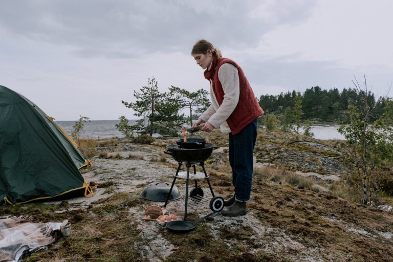 A Woman Cooking on a Charcoal Grill Near the Tent
