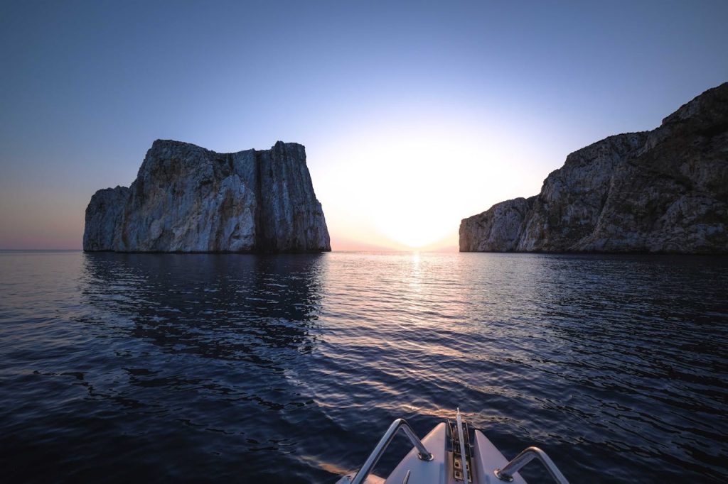 Rough cliffs in ocean with motorboat at sunset