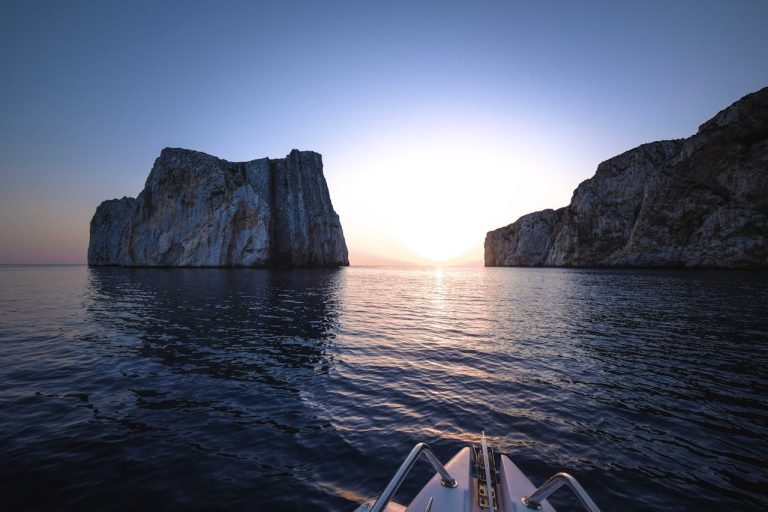 Rough cliffs in ocean with motorboat at sunset