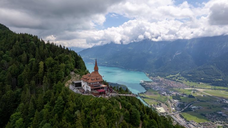 Brown and White Concrete Building Near Green Trees and Body of Water Under White Clouds during